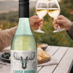 Bottle of Loose Moose wine with two glasses being held outdoors