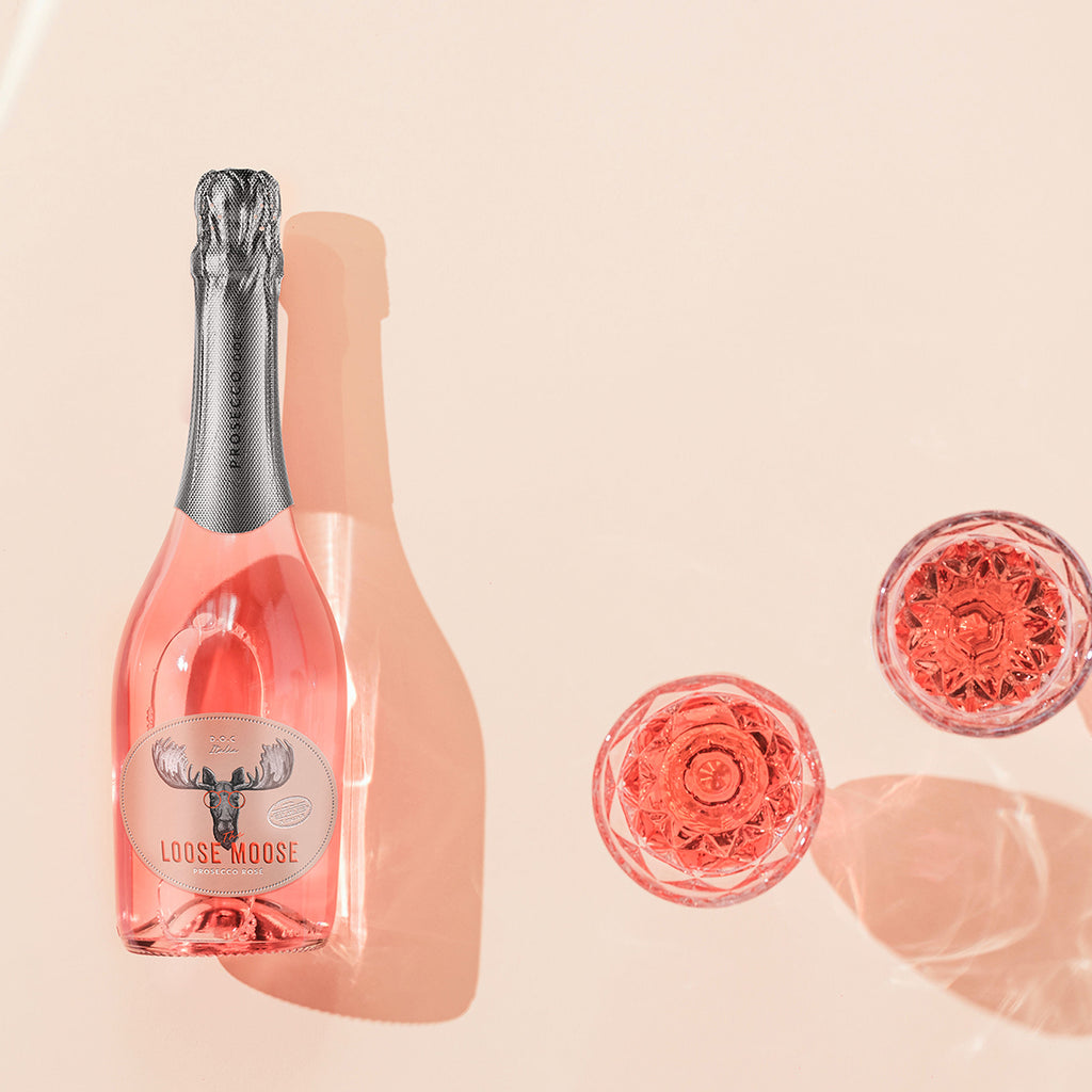 Pink bottle of Loose Moose sparkling wine with decorative glassware on a beige background